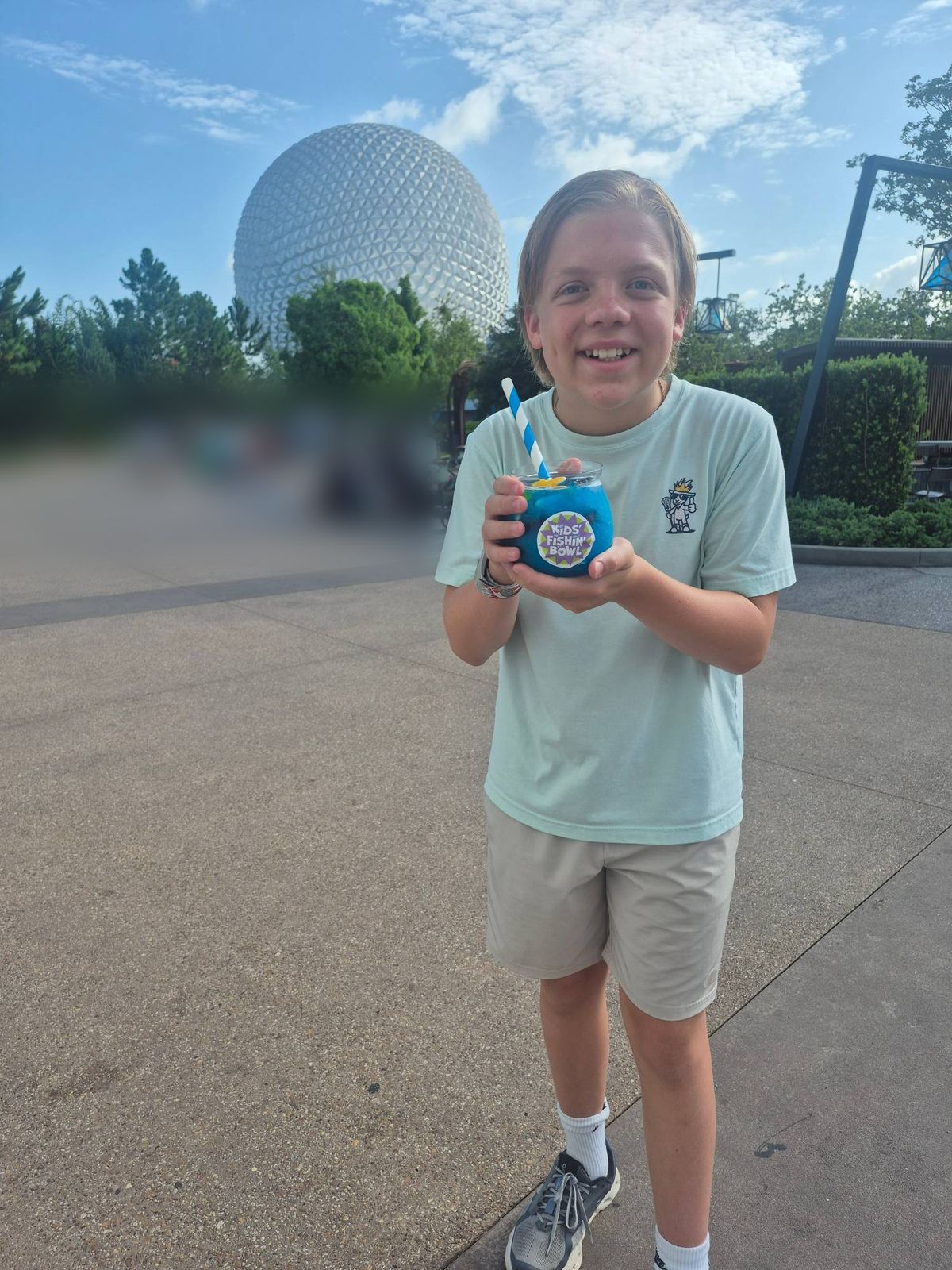 Henry holding a bright blue drink in front of the Epcot sphere
